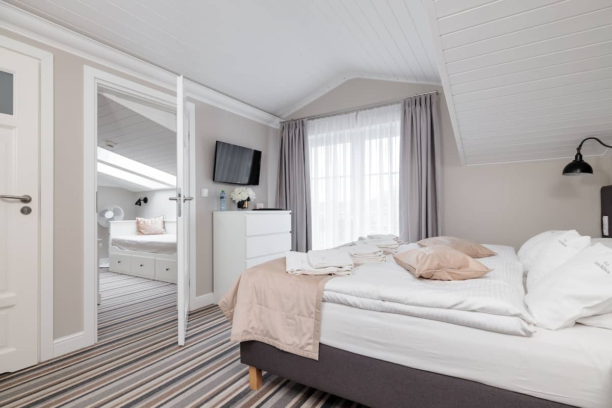 Un dormitorio con cama, televisor, cómoda y ventana con cortinas.