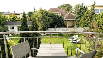 Een balkon met een tafel en twee stoelen, met uitzicht op een verzorgde tuin en omliggende huizen.