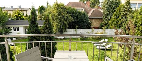 A balcony with a table and two chairs, overlooking a well-maintained garden and neighboring houses.
