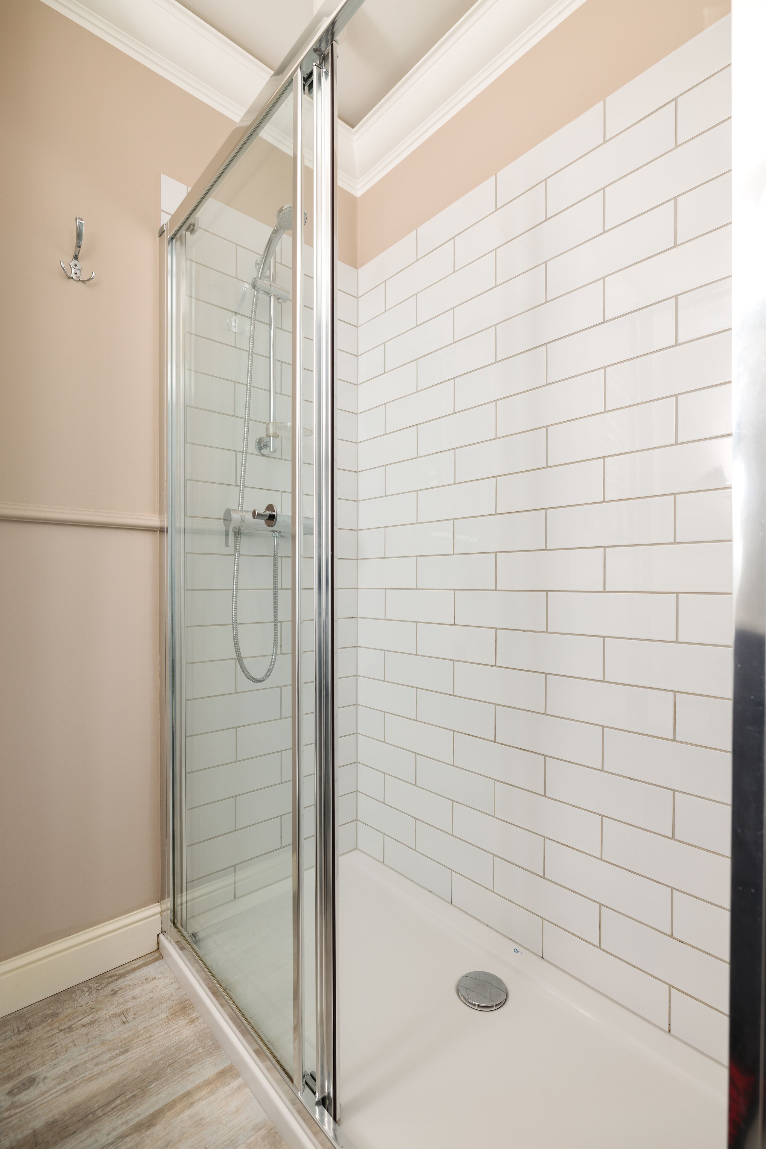 A glass-enclosed shower with white tiled walls and a wooden floor.