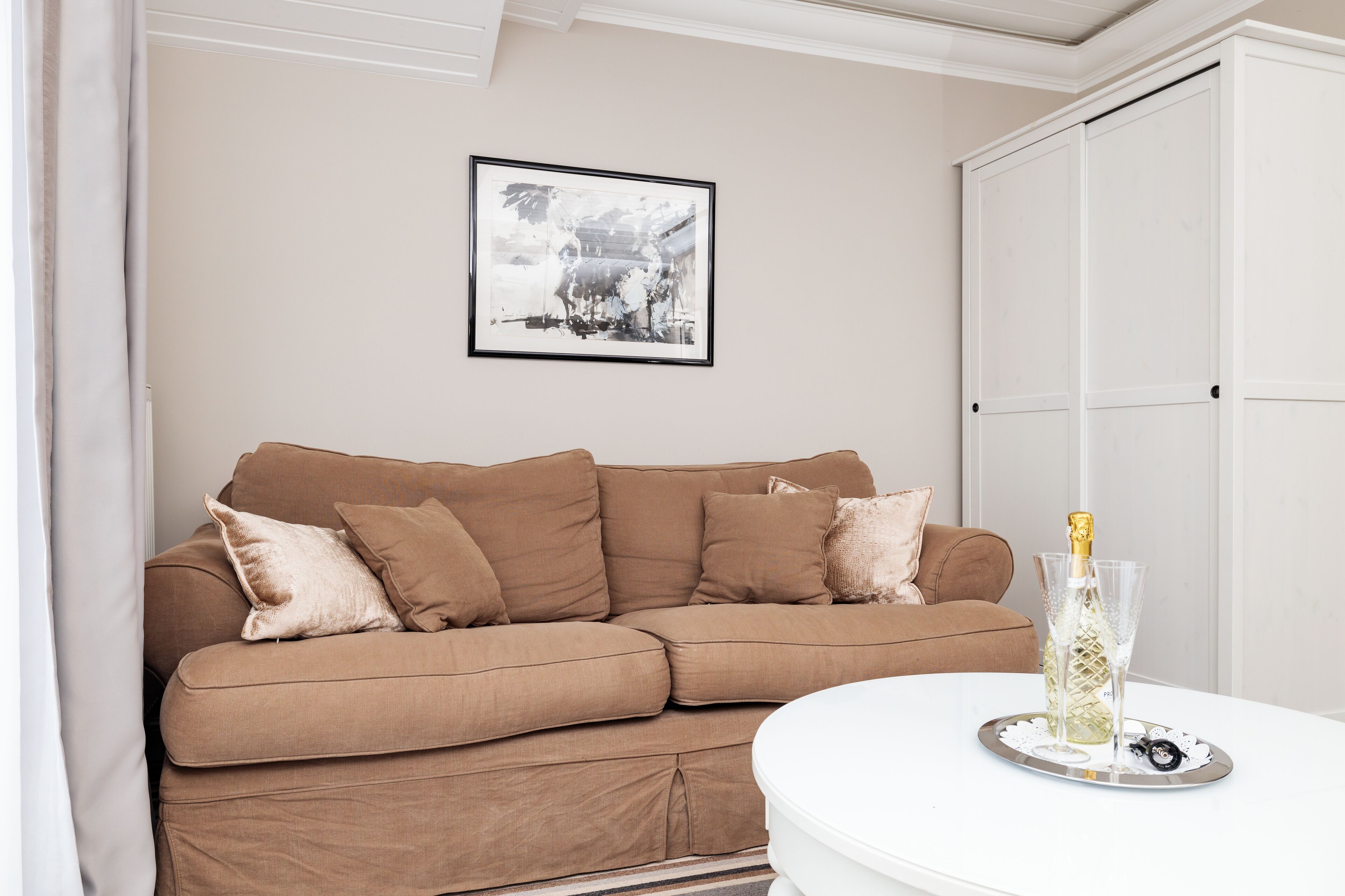 A brown sofa with cushions, a framed picture on the wall, and a bottle of champagne on a tray.