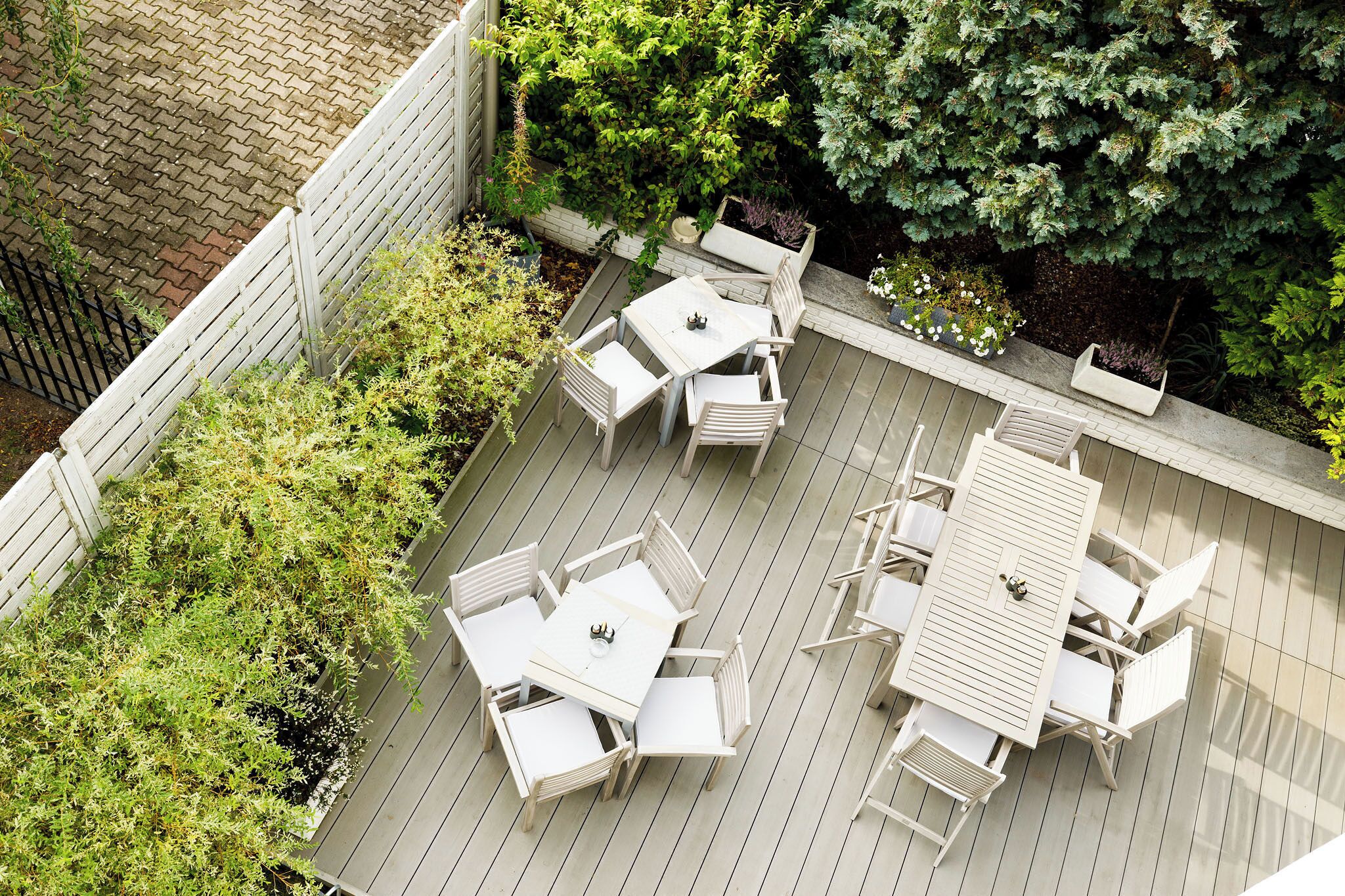 Una terraza con una mesa y sillas, rodeada de follaje y una cerca blanca.