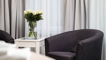 Una sala moderna con un sillón gris oscuro, una mesa de centro de vidrio con un florero de flores blancas y cortinas blancas traslúcidas al fondo.