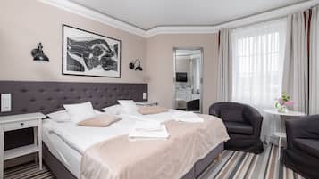 A hotel room with a large bed, two bedside tables, a chair, a small round table with a vase of flowers, a mirror, and artwork on the wall.