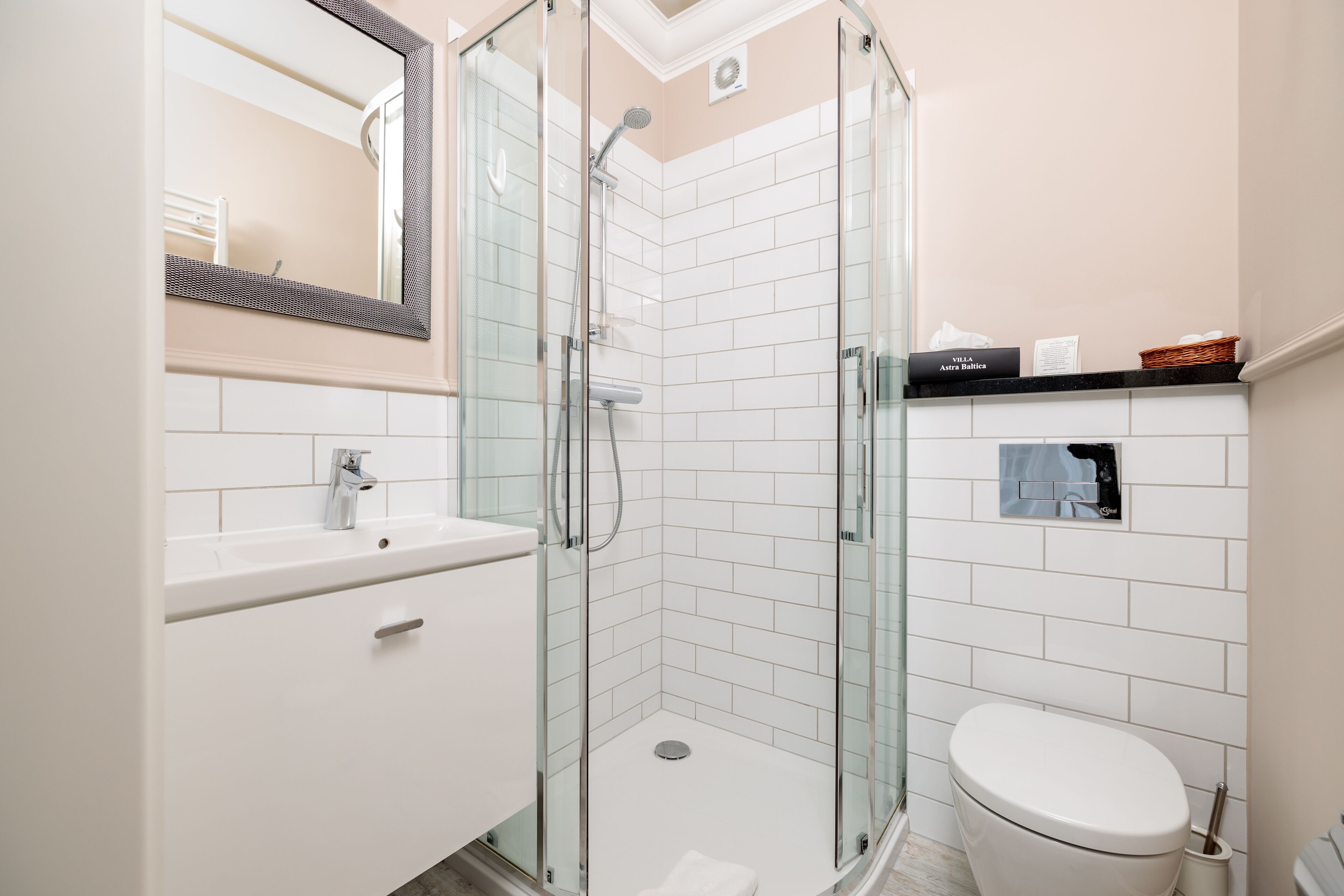 Un bagno moderno con doccia vetrata, piastrelle bianche, un lavandino bianco e un water.