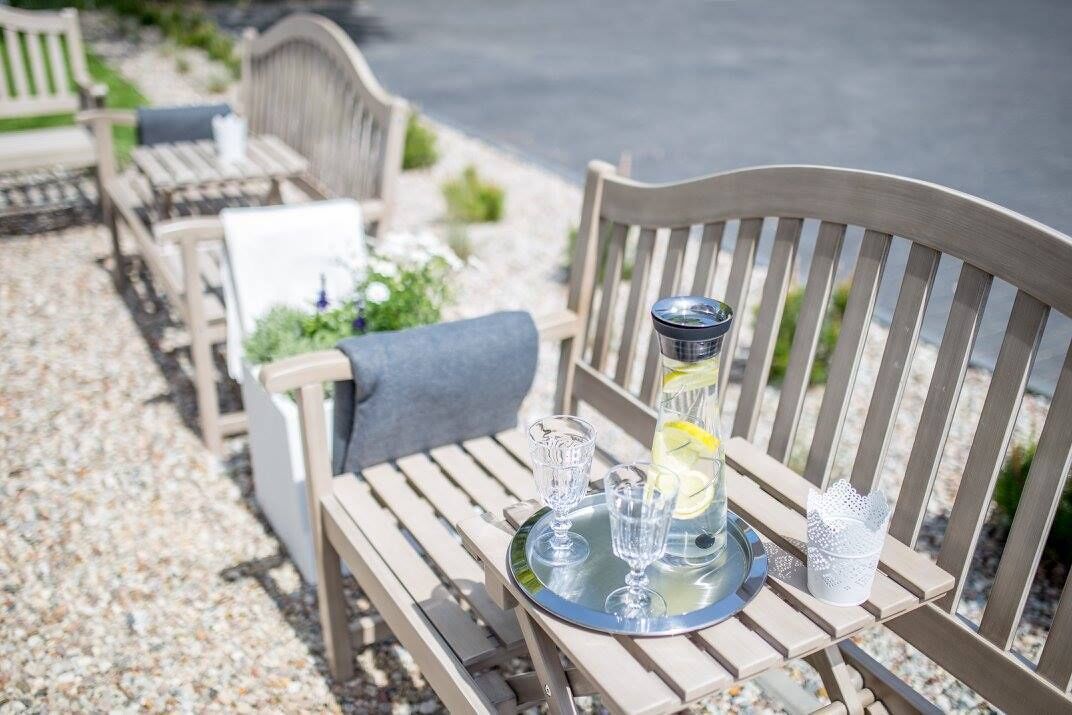 A wooden bench with a tray holding a glass bottle, two glasses, and a small decorative item.