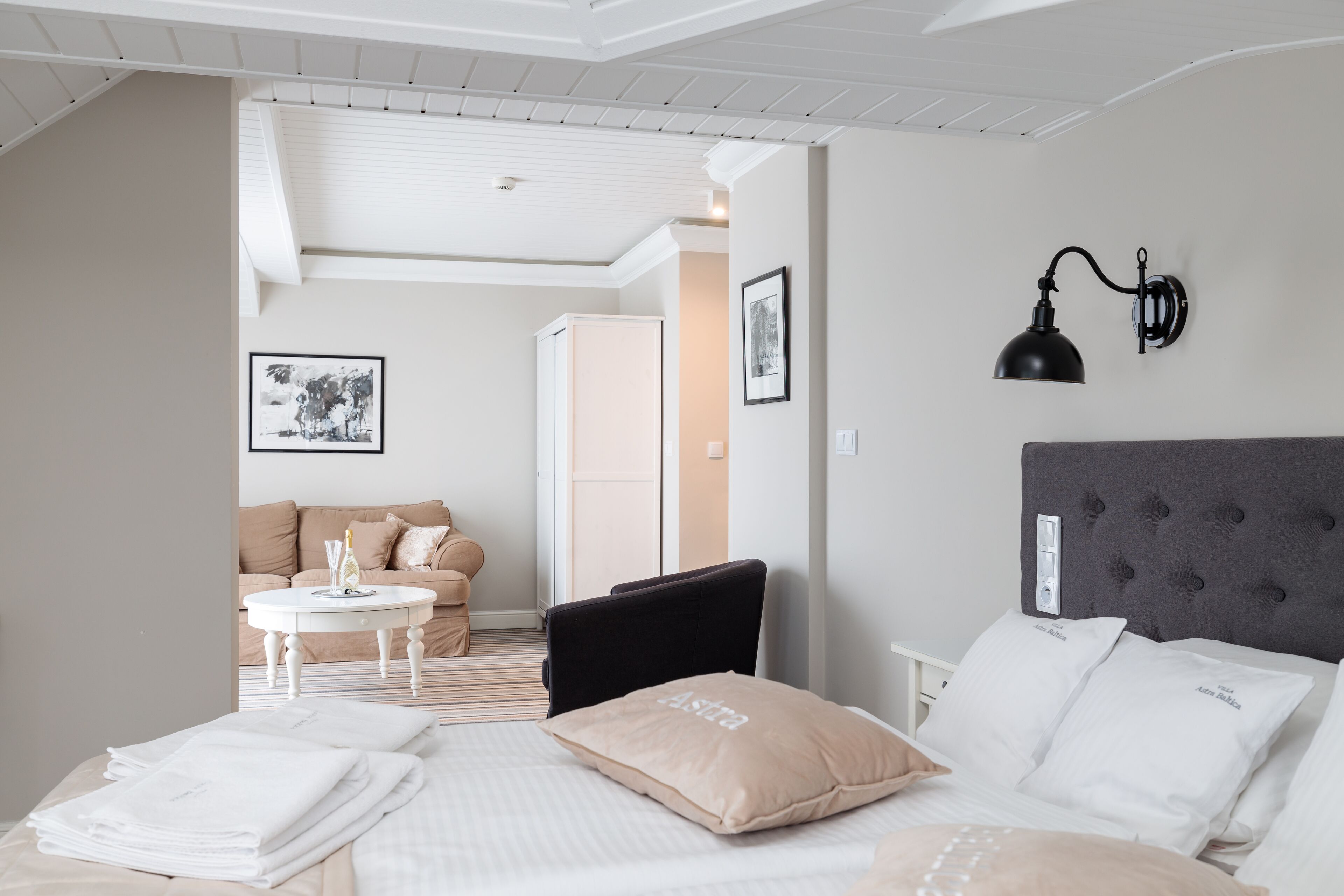 A hotel room with a bed, a small round table, a sofa, and a wall-mounted lamp.