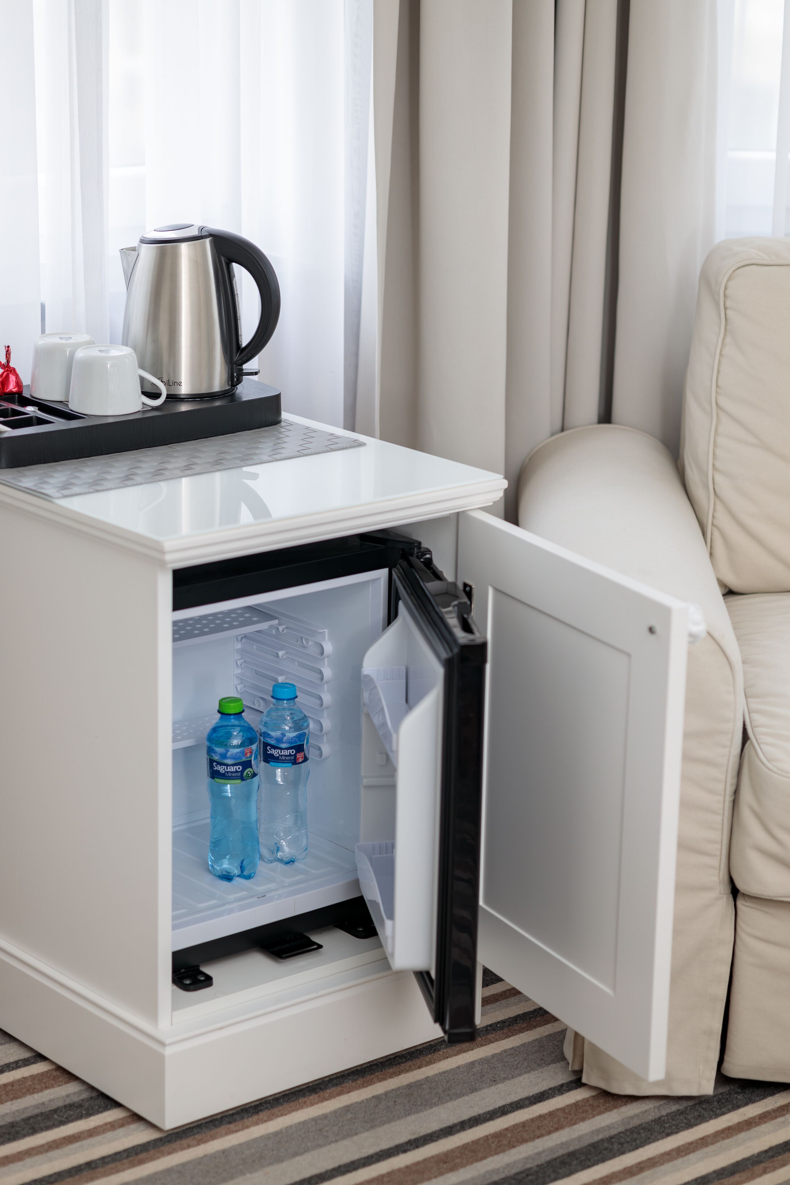 A compact minibar with a kettle, two water bottles, and a coffee maker.