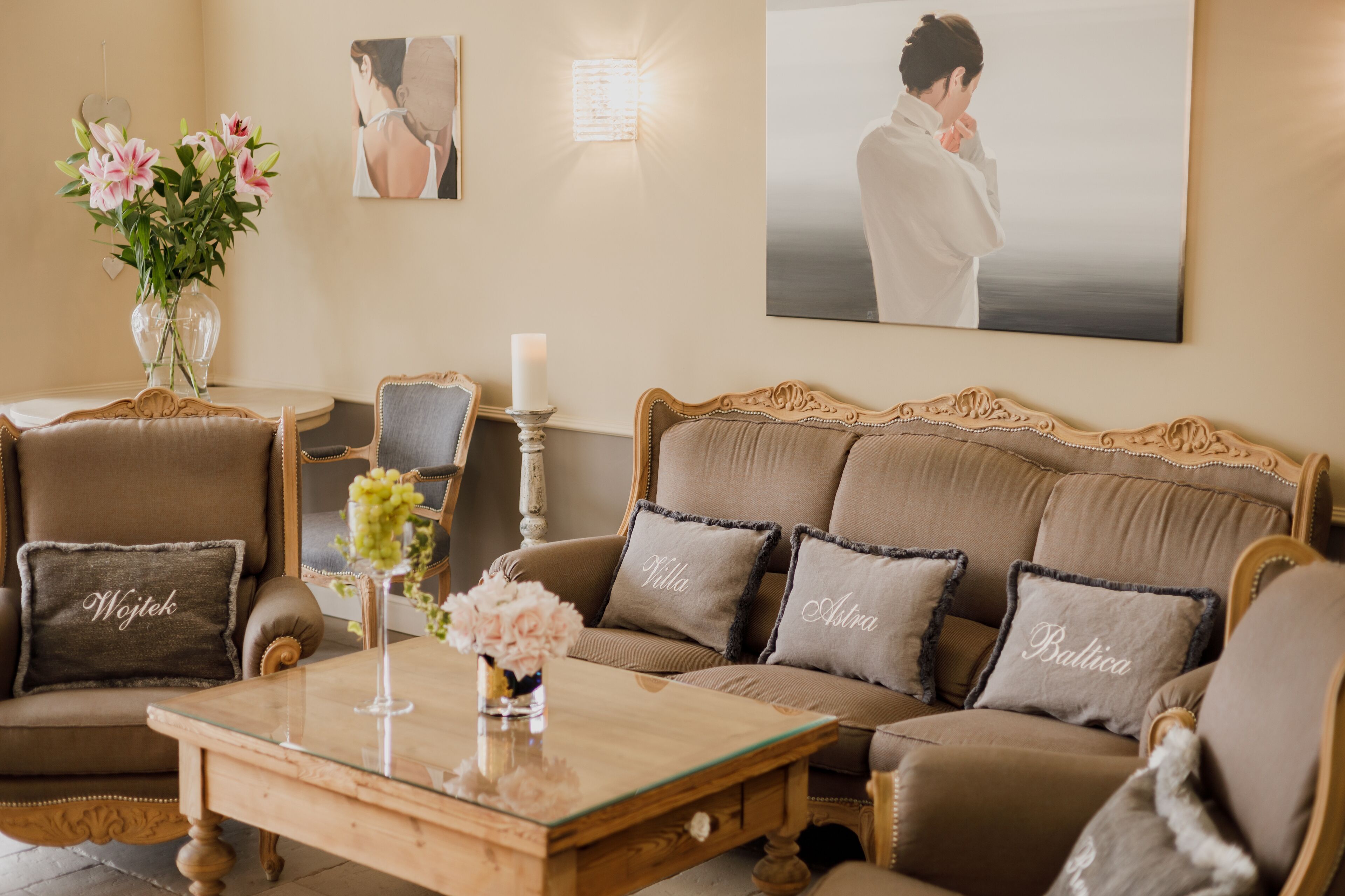 Un salon chaleureux avec un canapé marron, deux fauteuils, une table basse en verre et un vase rempli de fleurs.