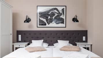 A neatly made double bed with white linens and two beige pillows, a dark tufted headboard, and two bedside tables with black wall lamps.