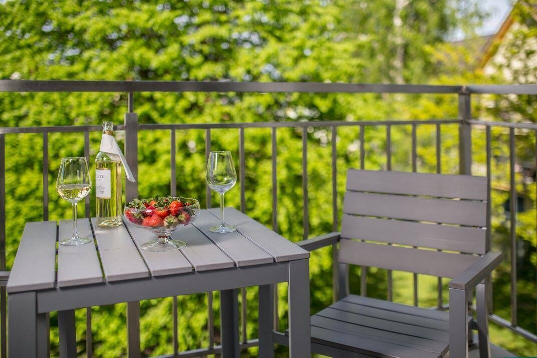 A balcony with a table set for two, a bowl of fruit, and two wine glasses.