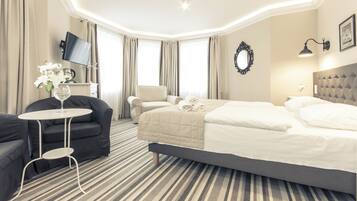 A hotel room with a bed, a sofa, a small table, a TV, and a window with curtains.