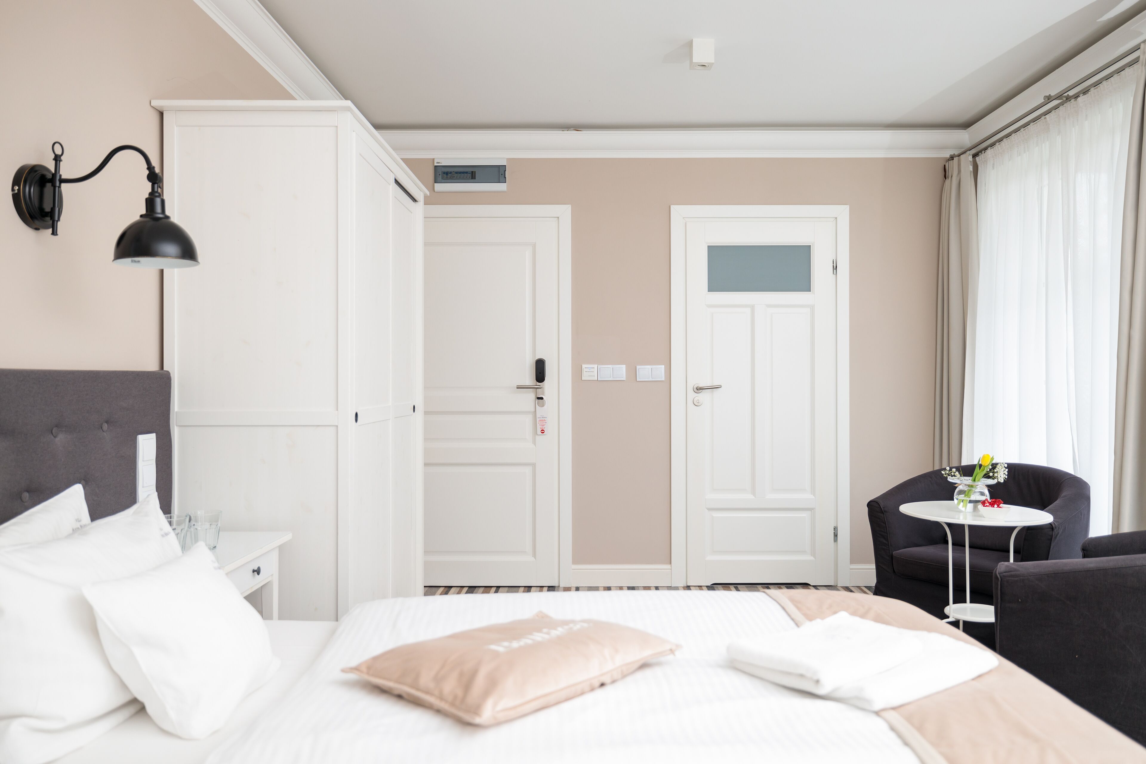 A hotel room with a bed, a nightstand, a wardrobe, a desk, a chair, a small table, and a door.