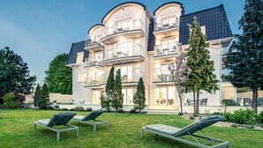 Un hotel de varios pisos con balcones, un césped bien cuidado y mobiliario exterior.