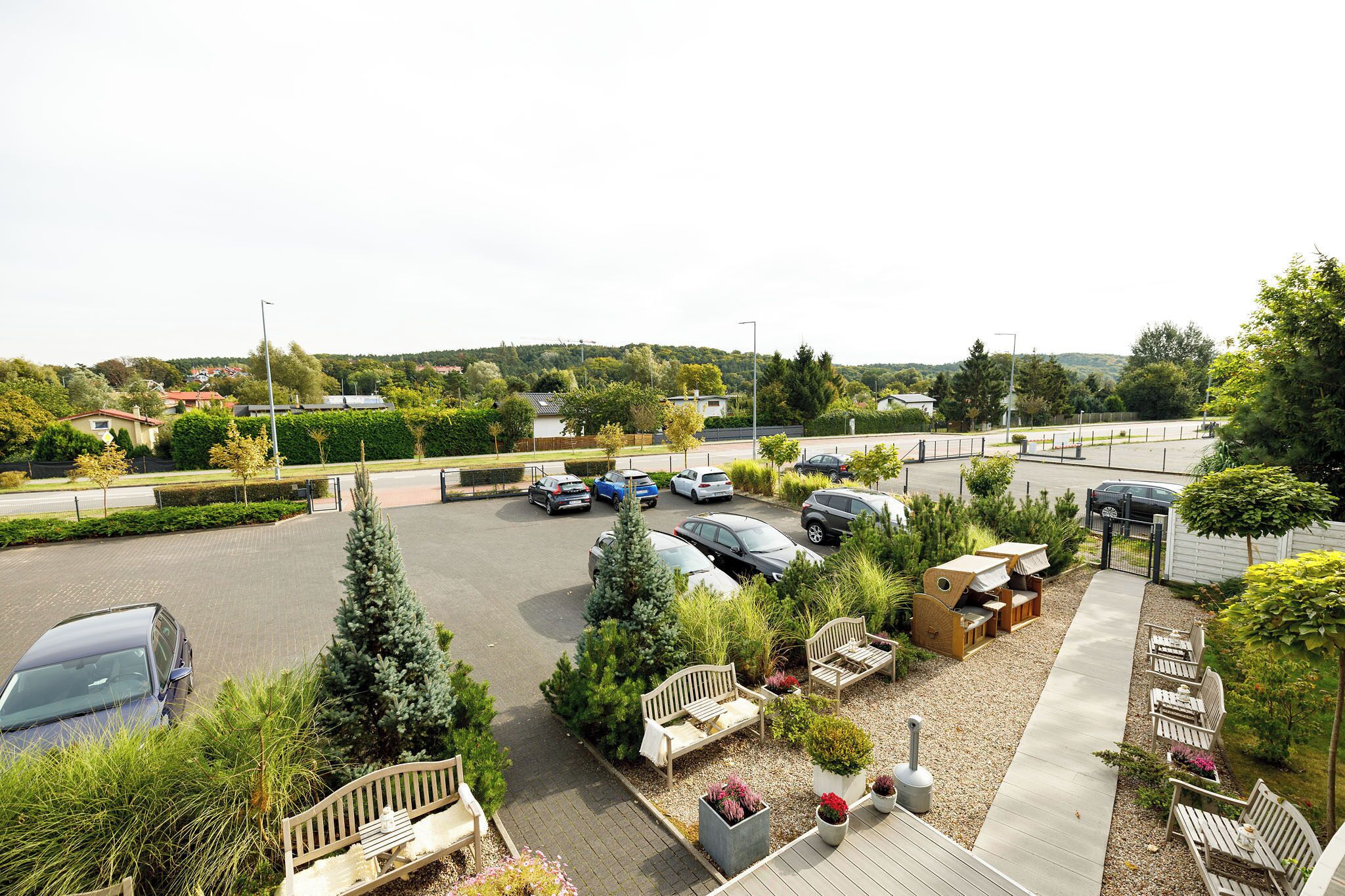 A parking lot with cars, a covered seating area, and a view of a residential area with houses and trees.