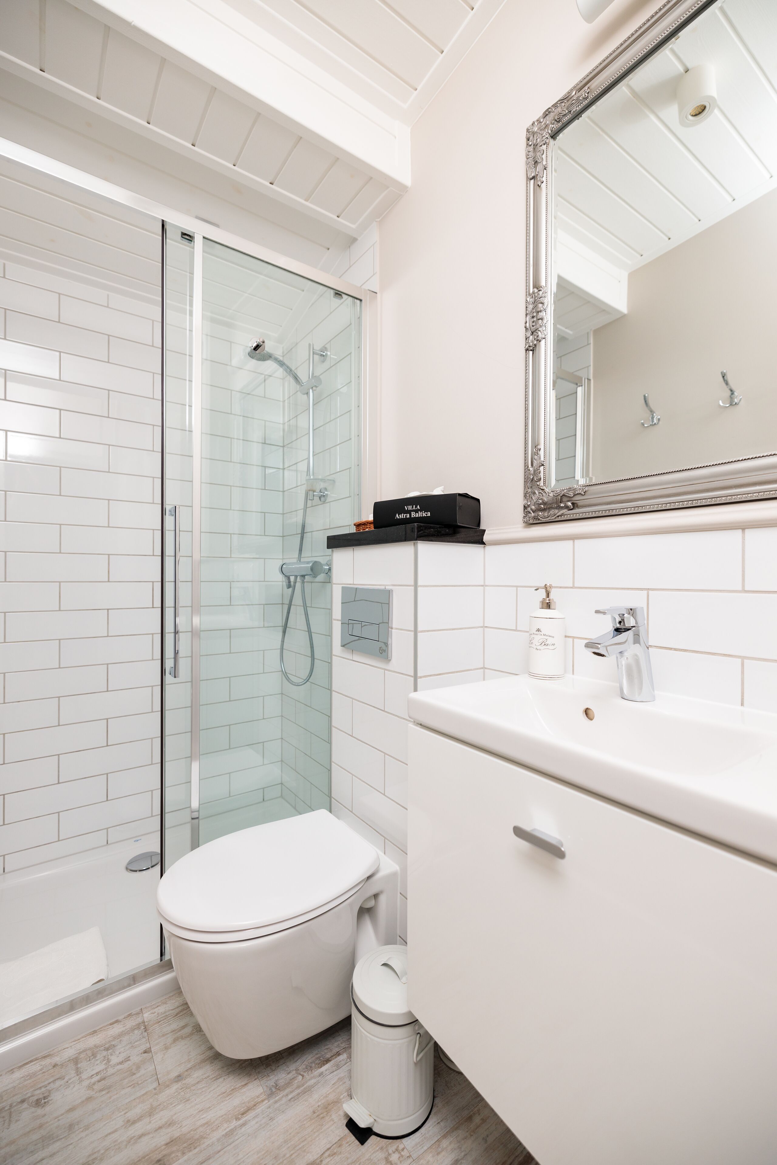A modern bathroom with a glass-enclosed shower, a white toilet, a vanity with a mirror, and a bottle of hand soap.