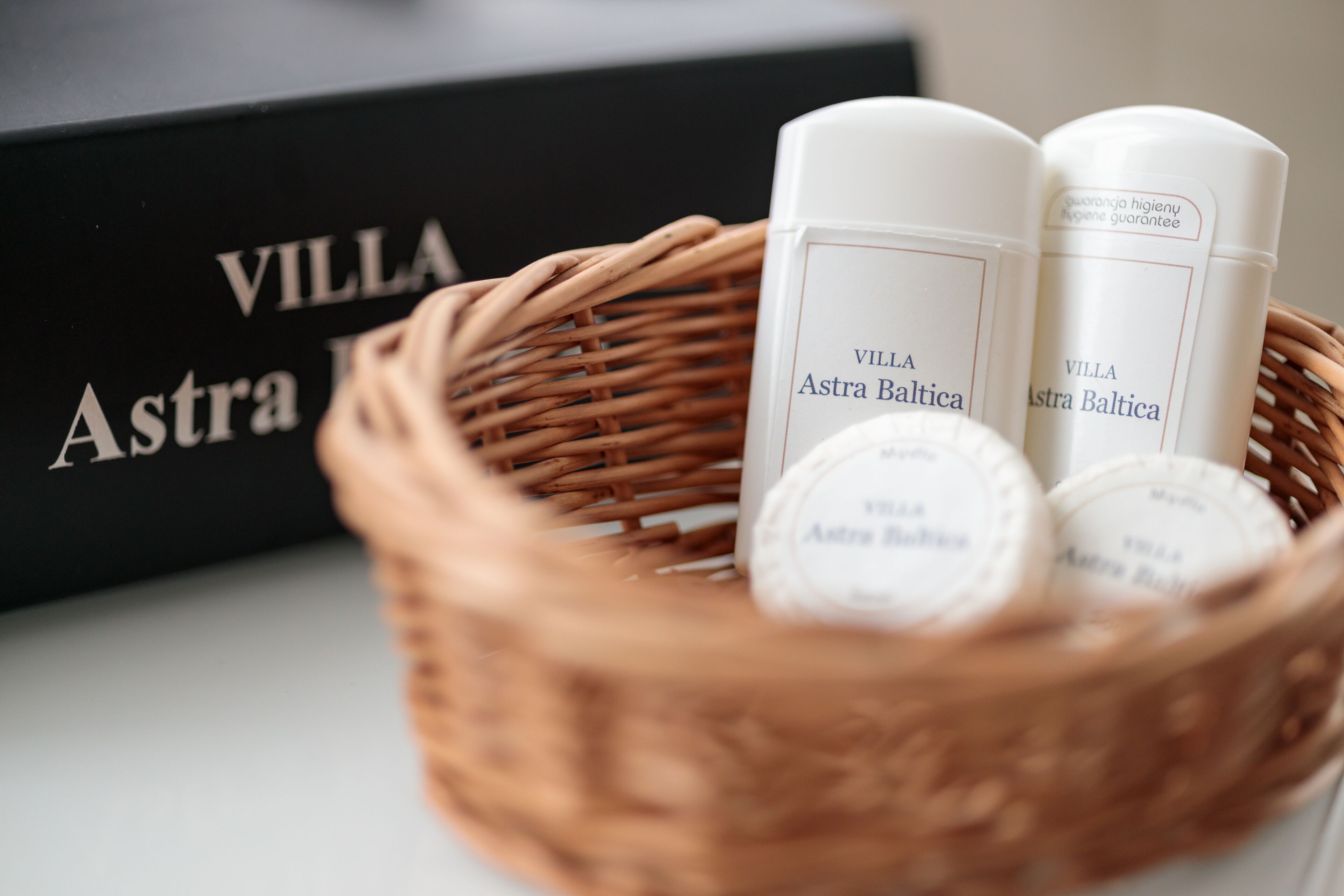 Una cesta de mimbre con tres botellas blancas etiquetadas 'VILLA Astra Baltica' y una caja negra con el mismo nombre.