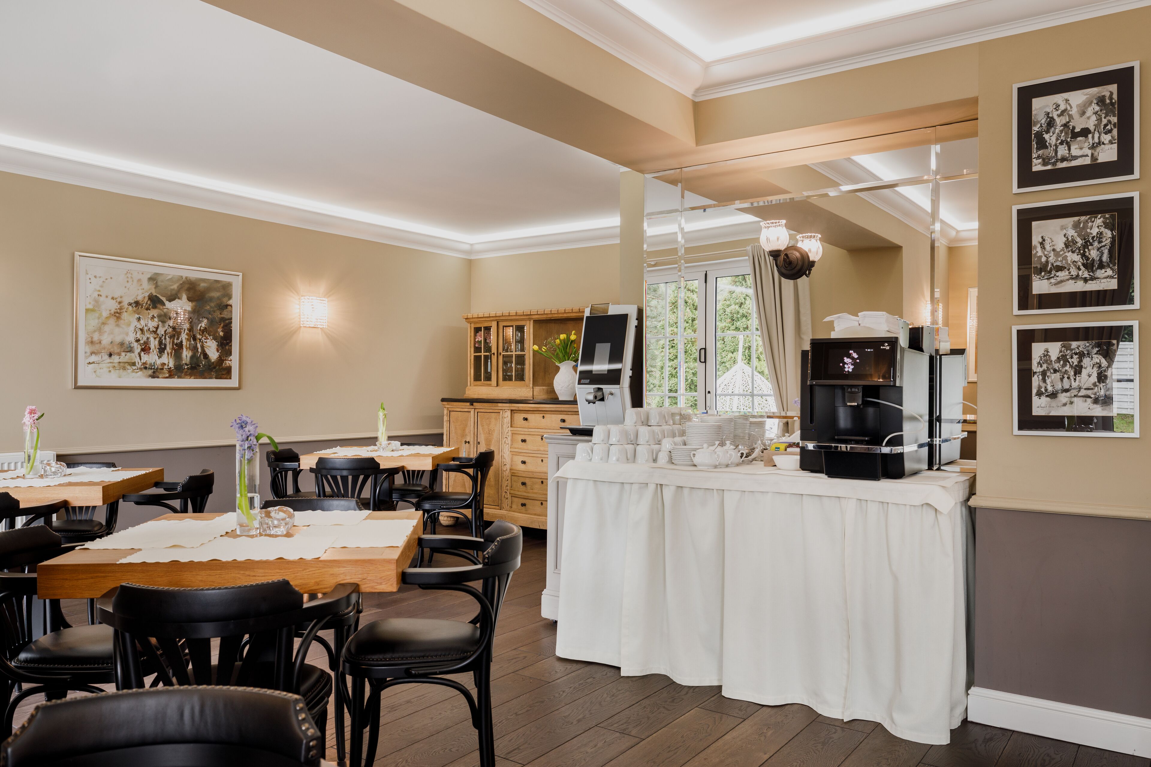 Un espace repas avec un buffet, des tables en bois, des chaises noires et une nappe blanche.