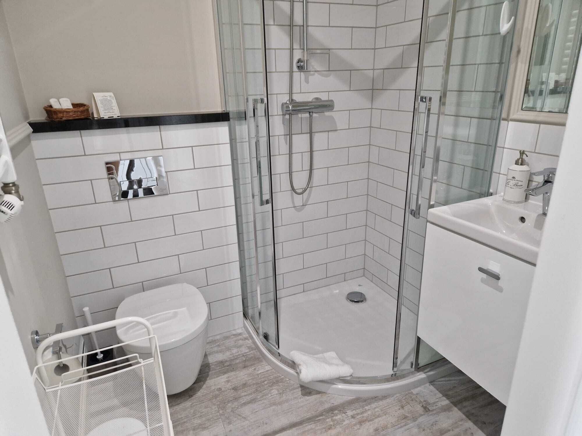 Ein modernes Badezimmer mit einer gläsernen Duschkabine, einer weißen Toilette und einem Waschbecken mit Spiegel darüber.
