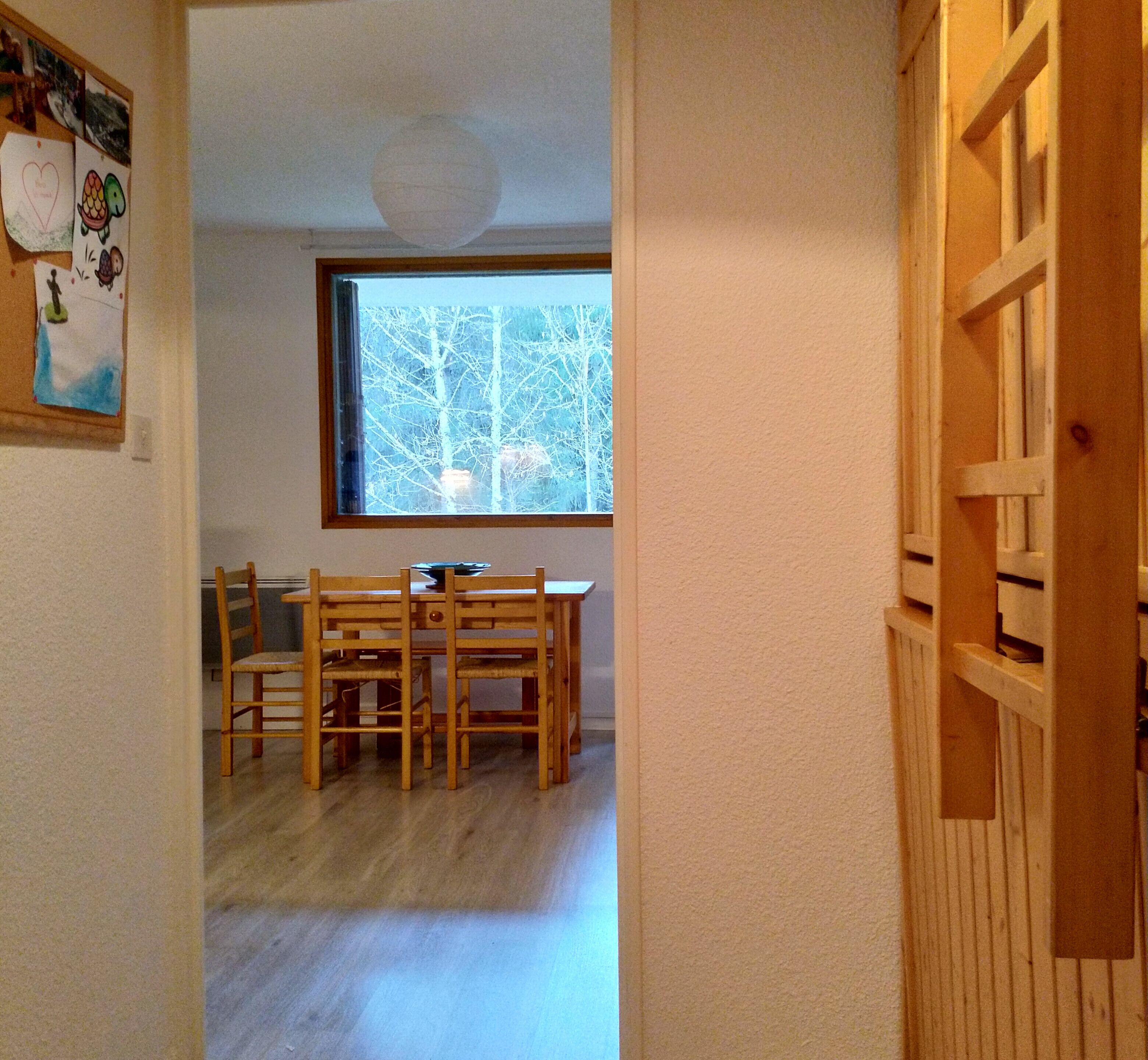 A room with a wooden dining table and chairs, a window with a view of trees, and a door with a wooden lattice design.