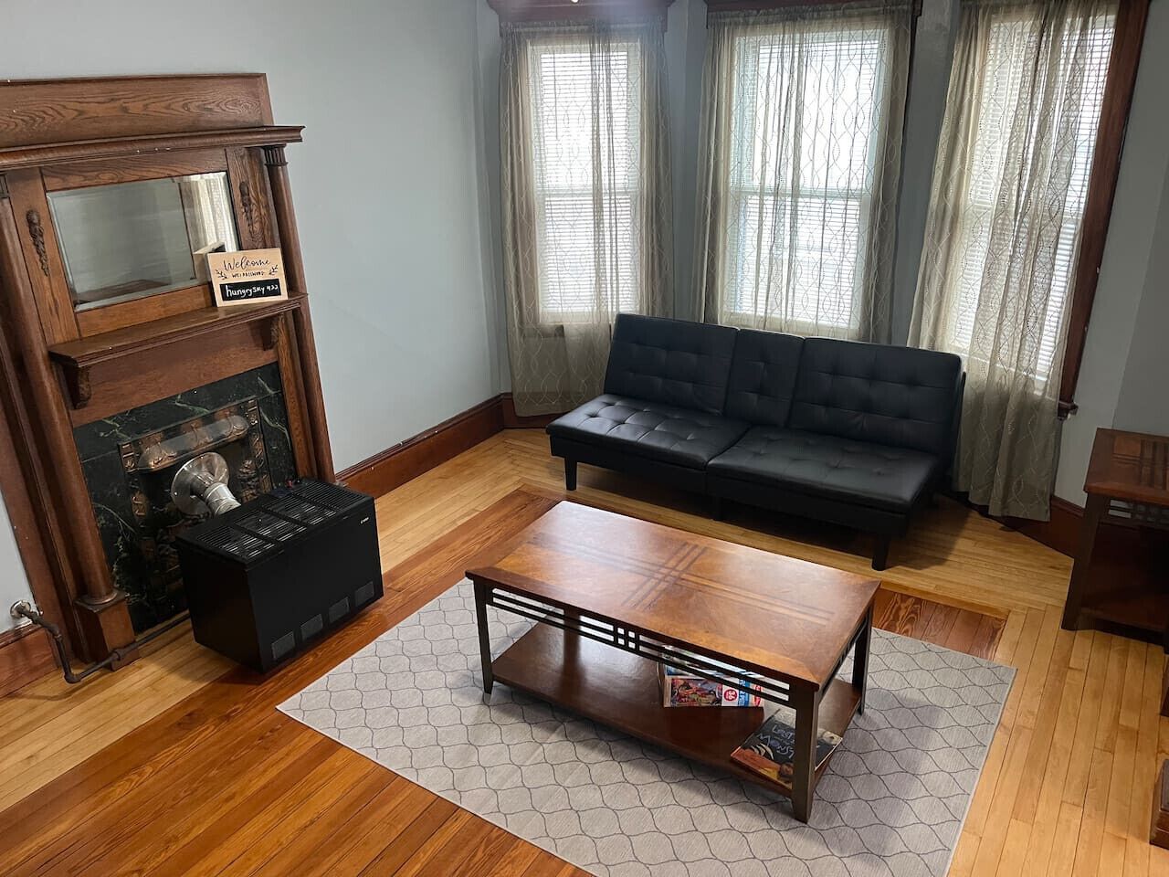 A living room with a wooden coffee table, a black sofa, and a fireplace with a sign.