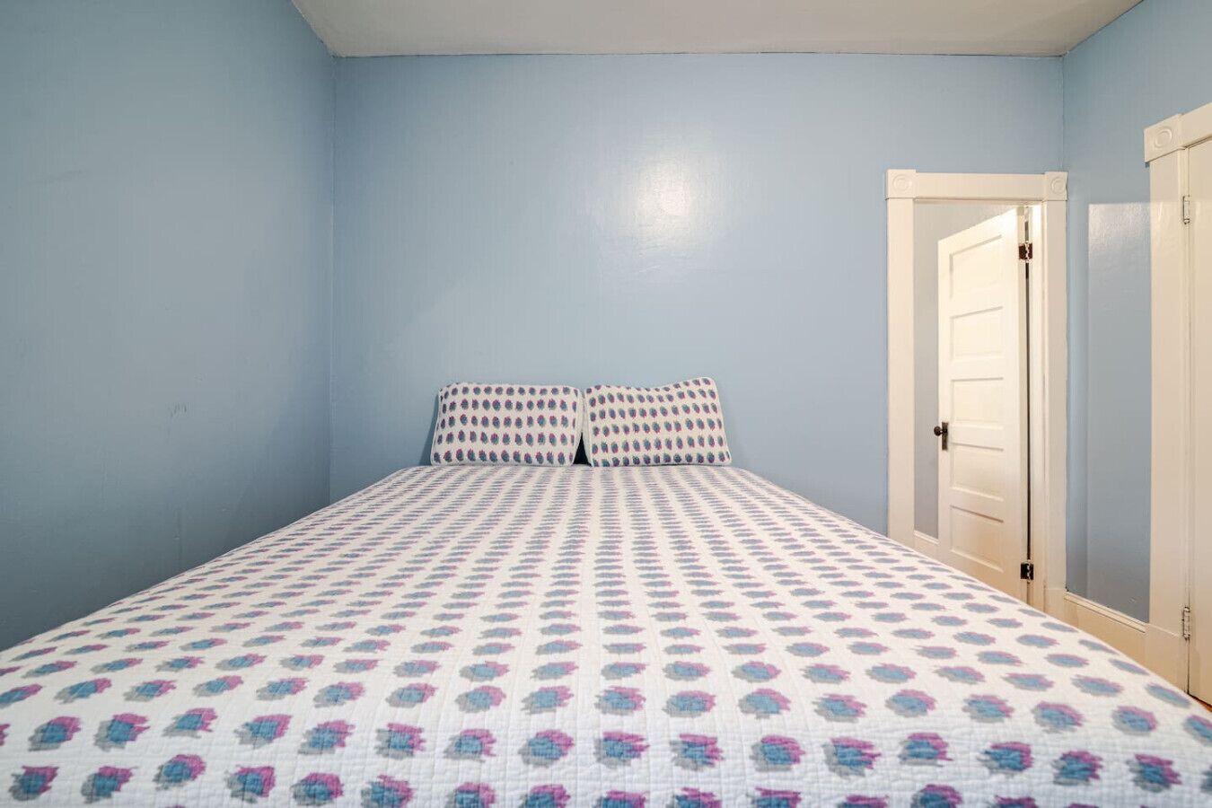 A bedroom with a bed, two pillows, and a door.