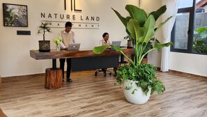 A reception area with a wooden floor, a reception desk, two employees at workstations, a large potted plant, and a chandelier. - KSol Hotel & Apartment (Cam Ly - Da Lat)