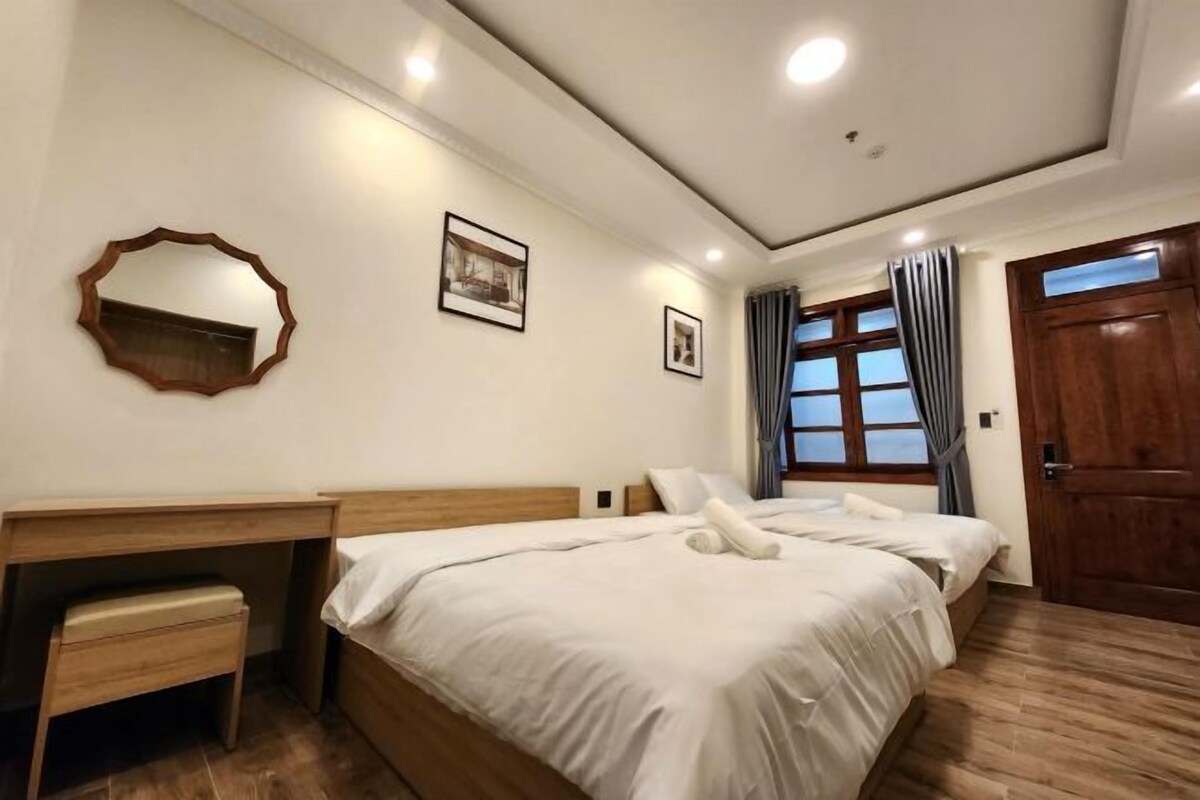 A hotel room with a large bed, a wooden desk, a small bench, and a door.