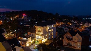 A town at night with a prominent building featuring a large central window and multiple balconies. - KSol Hotel & Apartment (Cam Ly - Da Lat)