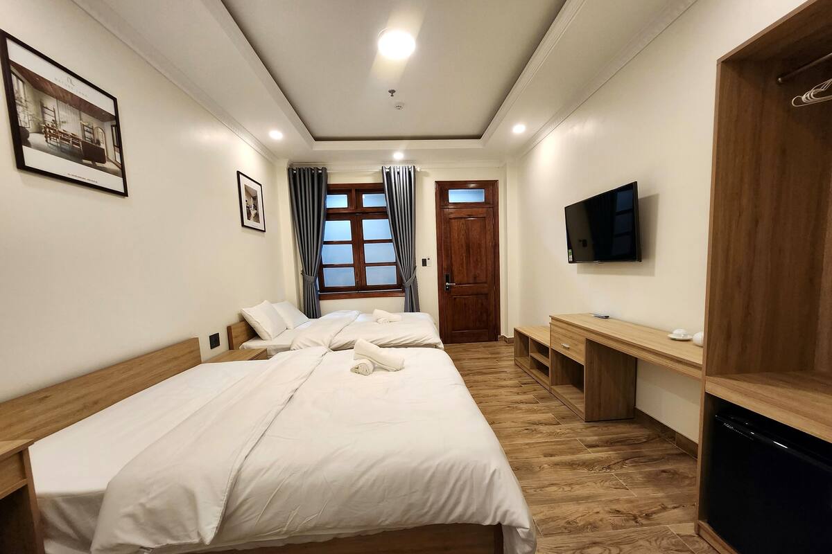 A hotel room with a large bed, a wooden desk, a television, and a door leading to another room.