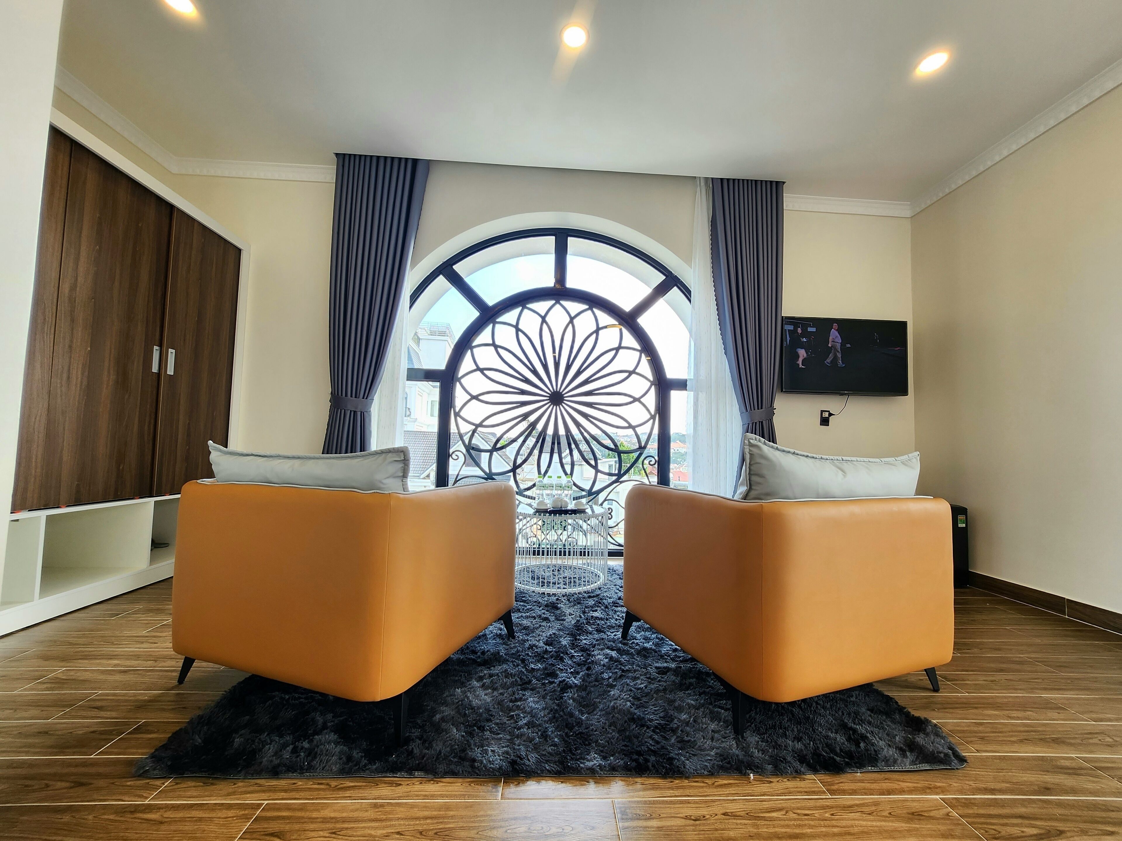 A modern room with a large window, two orange chairs, a black furry rug, and a wooden wardrobe.
