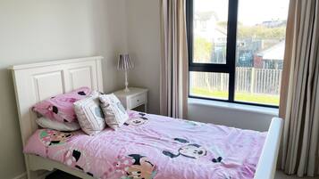 A bedroom with a bed featuring a pink Minnie Mouse themed bedspread, a white headboard, and a nightstand with a lamp.