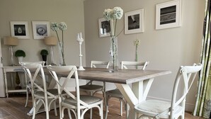 A dining area with a wooden table, white chairs, and framed pictures on the wall.
