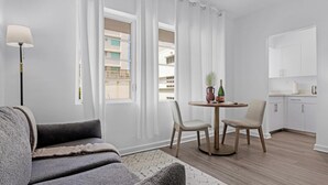Un salon moderne avec un canapé, une table à manger et des chaises, une lampe, et une vue sur l’extérieur.