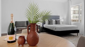 Une chambre d’hôtel avec un lit, un canapé, une table sur laquelle se trouve une bouteille de champagne, un vase et une plante en pot.