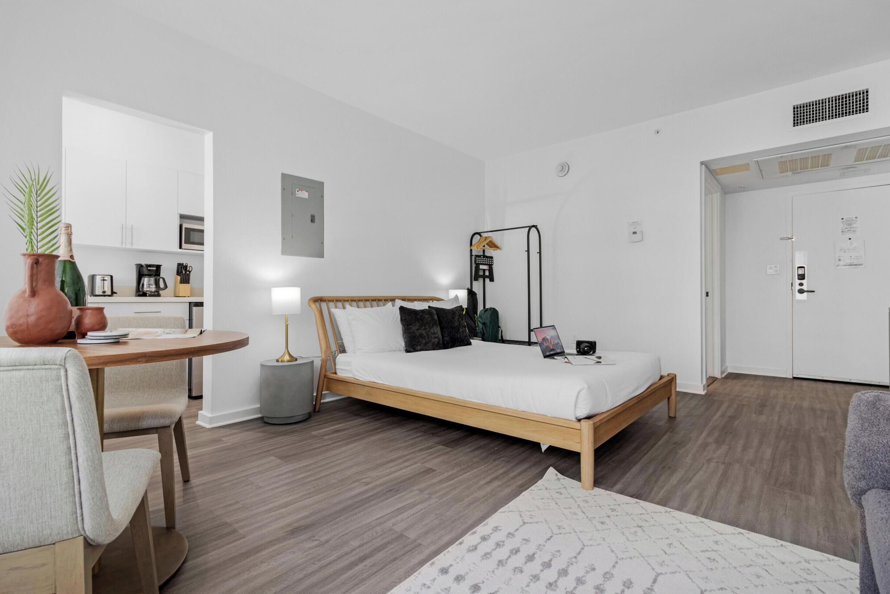 A modern, well-lit bedroom with a wooden bed, a bedside table, and a small desk area with a chair.