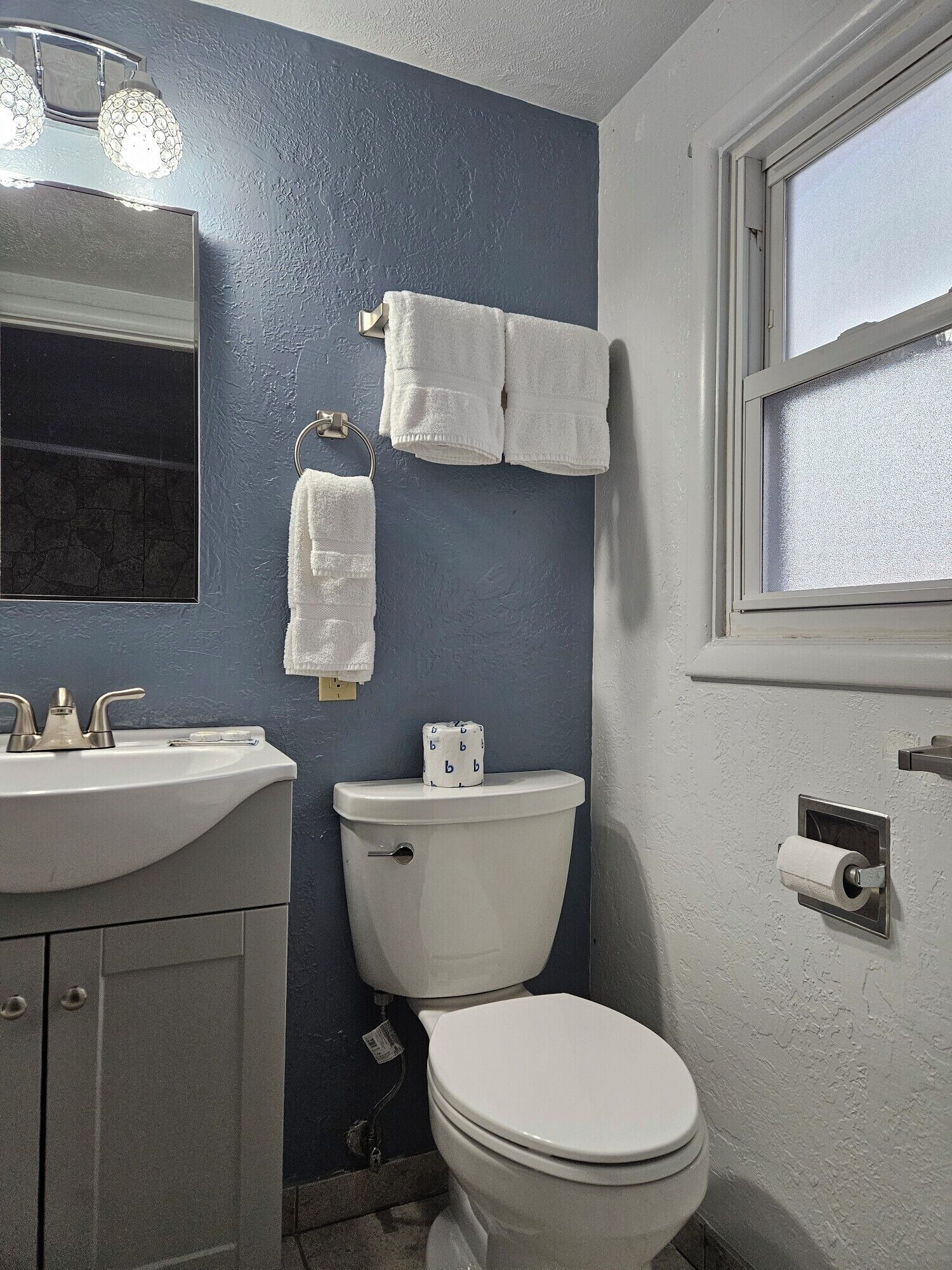 A bathroom with a sink, toilet, and a window.