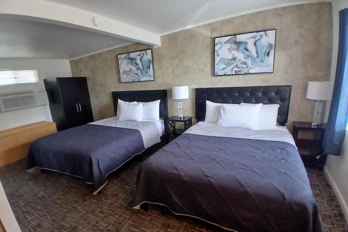 Quarto de hotel com duas camas, um guarda-roupa, obras de arte nas paredes e piso coberto de carpete.