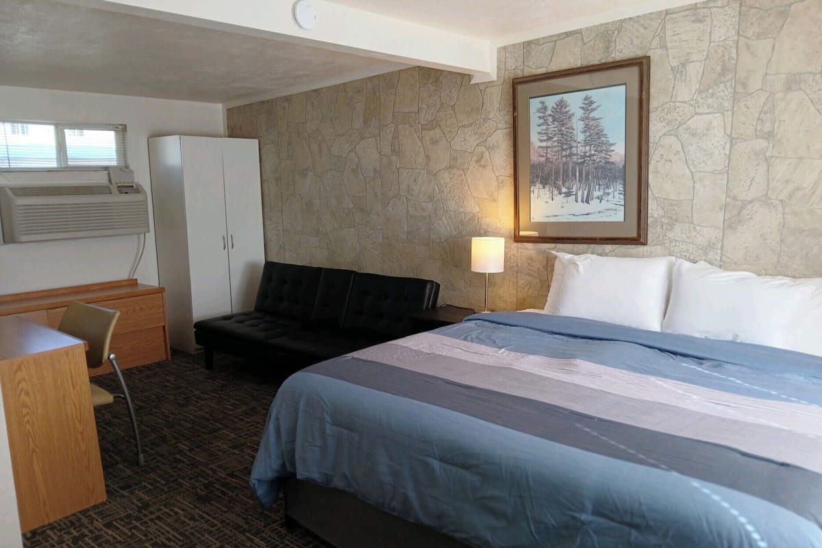 Quarto de hotel com cama, escrivaninha, cadeira, guarda-roupa e um quadro na parede.