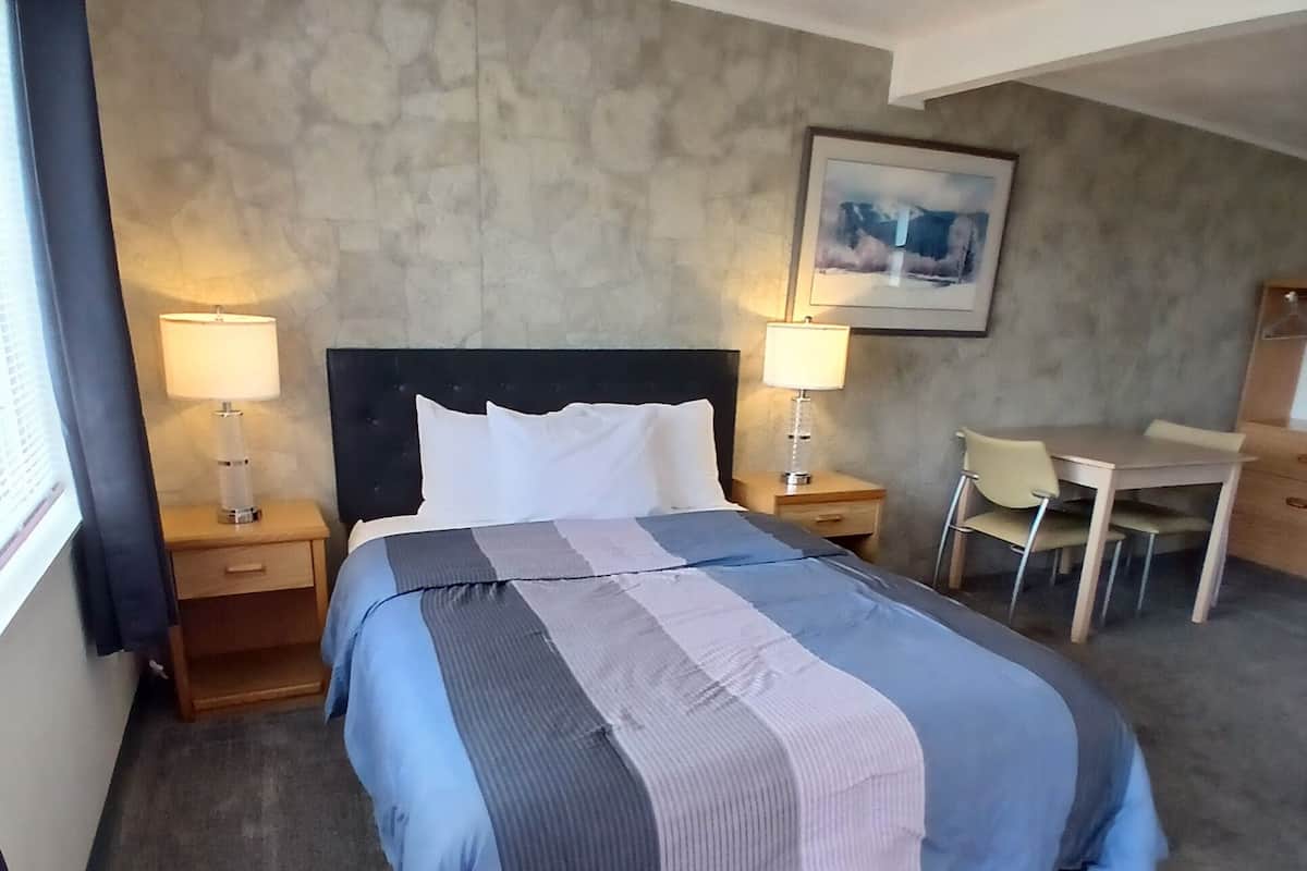 Quarto de hotel com uma cama, duas mesas de cabeceira, uma escrivaninha e uma cadeira.