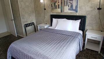Un dormitorio con cama, mesitas de noche, una silla, una puerta y un cuadro colgado en la pared.