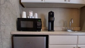A kitchen with white cabinets, a black microwave, a coffee maker, and a stainless steel refrigerator. - Silver Lakes Inn (Hayden)