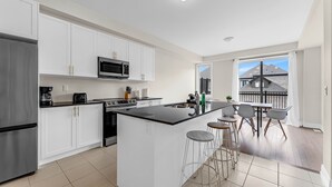 A modern kitchen with white cabinetry, a stainless steel refrigerator, a microwave, and a large island with stools.