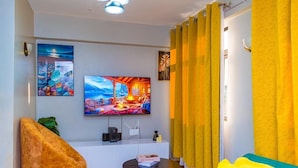 Een moderne woonkamer met een flatscreen televisie aan de muur, een comfortabele bank, een gele fauteuil en een klein bijzettafeltje.