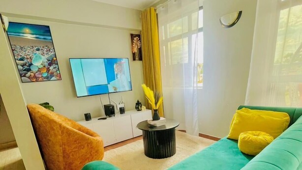 Een woonkamer met een groene bank, een klein rond bijzettafeltje, een televisie en een schilderij aan de muur.