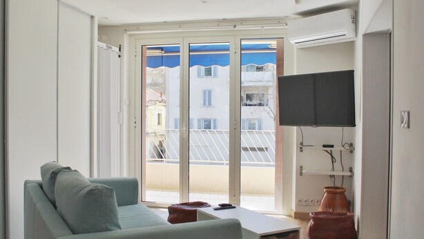 A modern living room with a sofa, a flat-screen TV mounted on the wall, and a sliding glass door leading to an outdoor balcony. - Spacious cocoon in Six-Fours-les-Plages (Six-Fours-les-Plages)