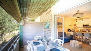 A dining area with a table set for four, a kitchen visible through an open door, and a covered outdoor seating area. - Comfortable apartment with pool (Moliets-et-Maa)