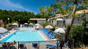 A swimming pool with lounge chairs and umbrellas, surrounded by trees and buildings. - Comfortable apartment with pool (Moliets-et-Maa)