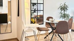 En matplats med ett runt bord, fyra stolar, en stor spegel, en vägglampa och en krukväxt.