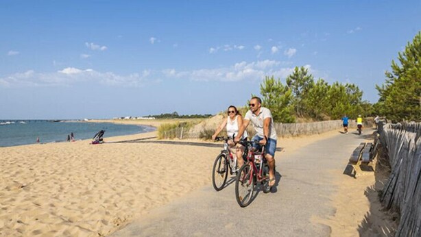 Una spiaggia sabbiosa con un vialetto lastricato, una recinzione in legno e un cielo azzurro limpido.